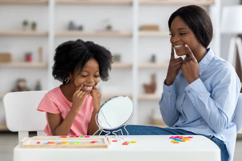 An SLP helping a young client work on their mouth shape to produce sounds
