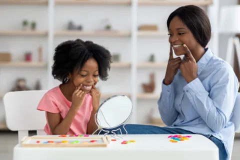 An SLP helping a young client work on their mouth shape to produce sounds