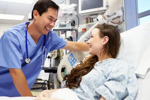 A smiling nurse treats a patient in a hospital bed.